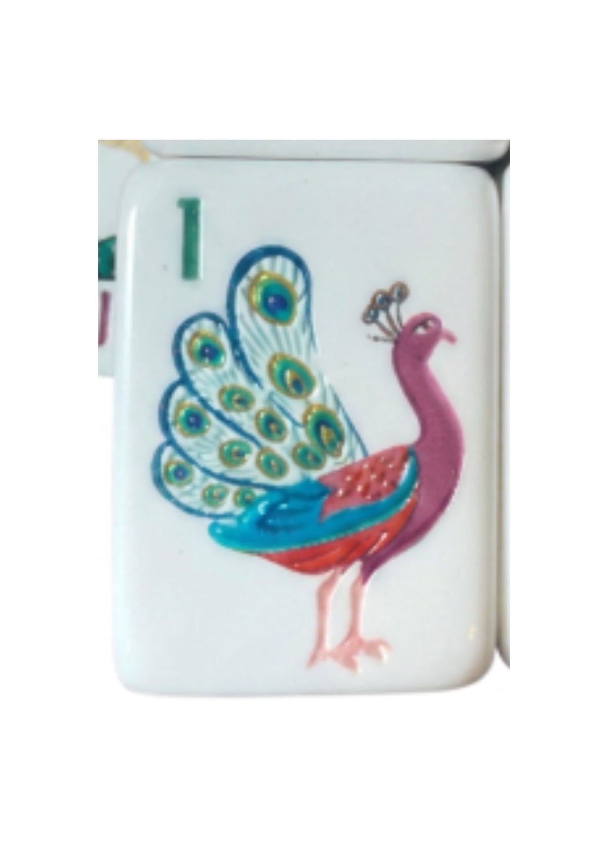 A white rectangular game piece or tile featuring a colorful painted peacock with blue, green, red, and pink details, plus a green number 1 on the left side.