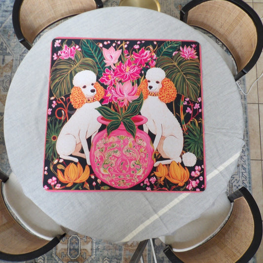 Black mahjong mat with two white poodles flanking a pink ginger jar of orchids and monstera leaves
