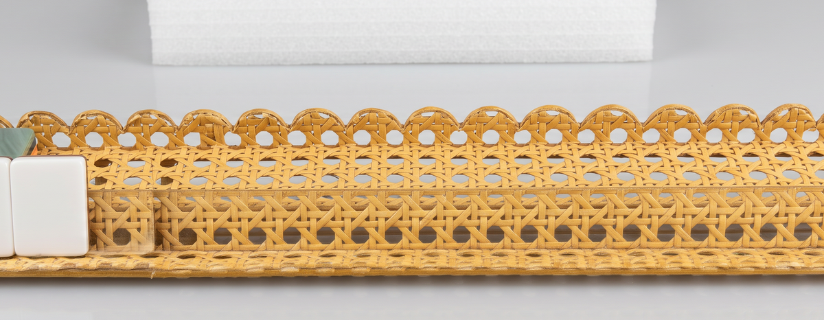 Side profile of the cane scalloped acrylic mahjong rack showing the scalloped pusher edge, woven cane inlay and a row of tiles
