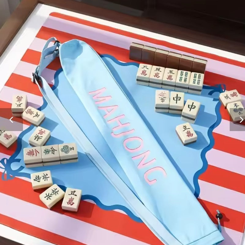 Luxury Mahjong light blue canvas mat bag with pink lettering and adjustable strap on a game table with mahjong tiles