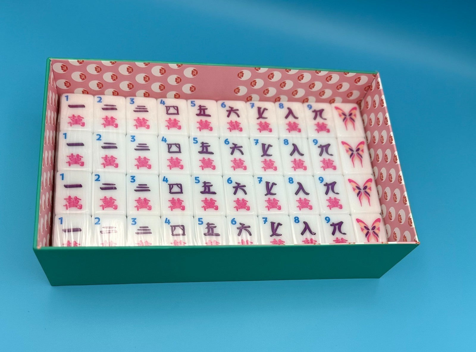 Luxury Mahjong teal box filled with white tiles featuring pink and blue Chinese characters and butterfly designs.