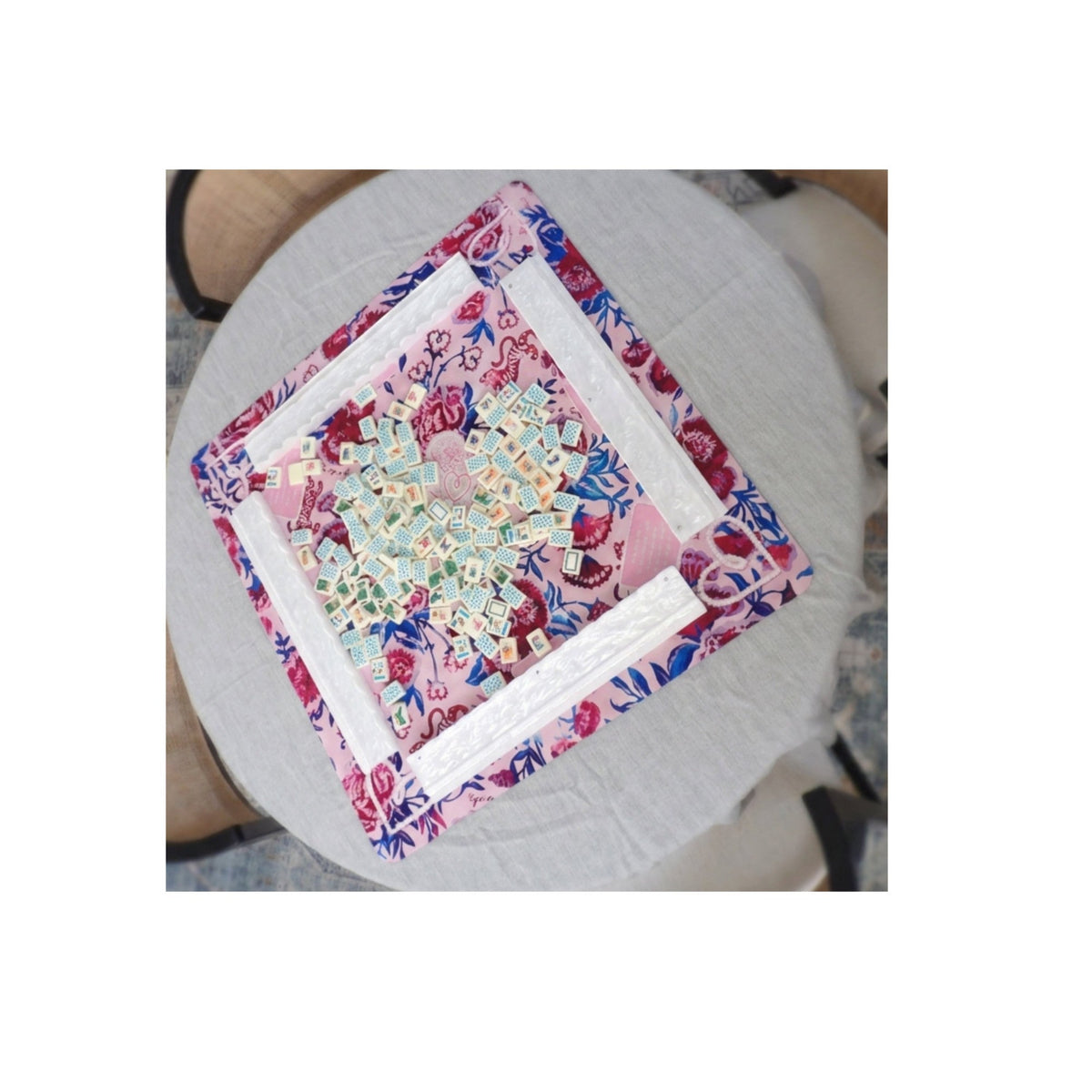 Luxury Mahjong tropical themed set with illustrated tiles on a pink floral mat and white tile racks on a round table.